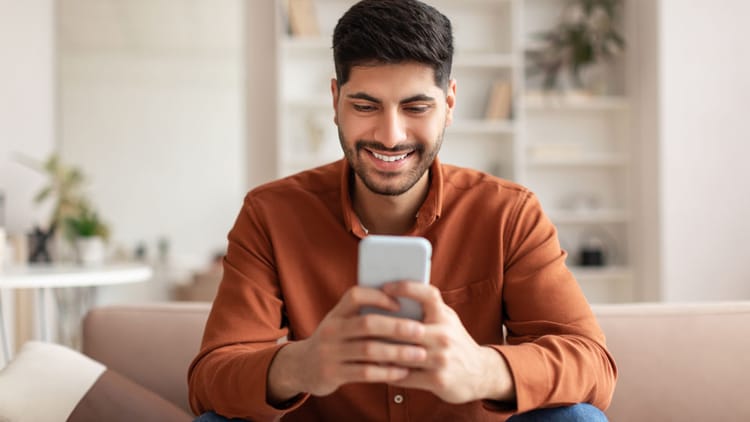 Man sitting at home smiling looking at phone.