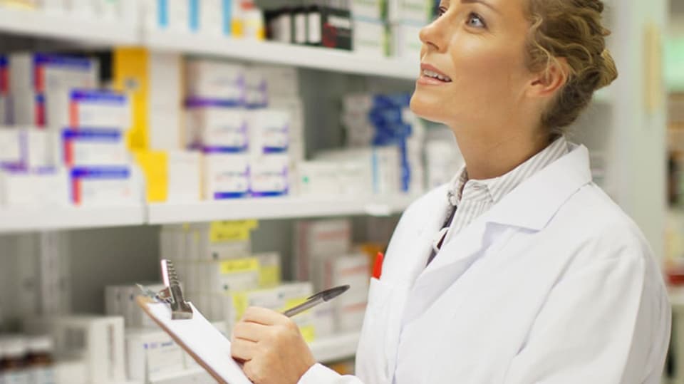 A pharmacist doing an inventory of a shelf of pharmaceutical medications.