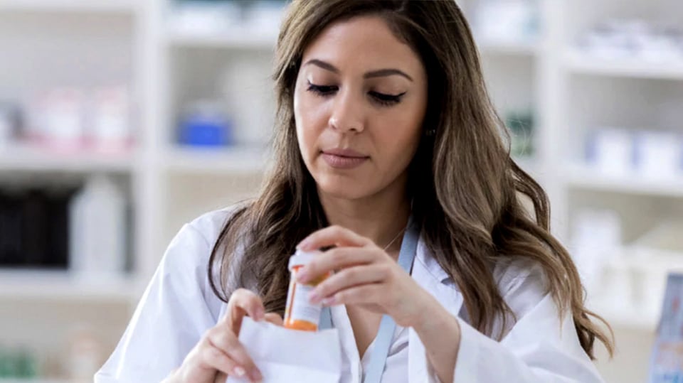 A pharmacist putting prescription into a bag.