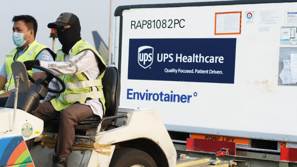 Two UPS workers transporting a cargo container of vaccines.