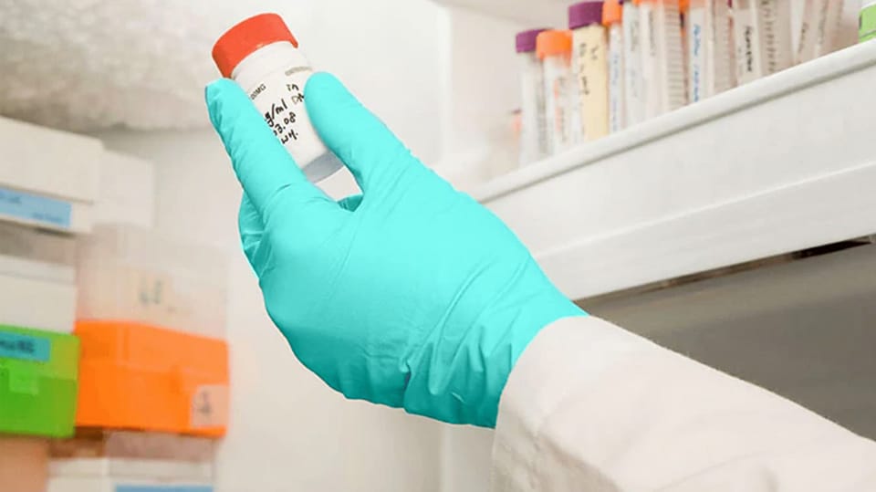 A gloved hand removing a lab specimen from a freezer.