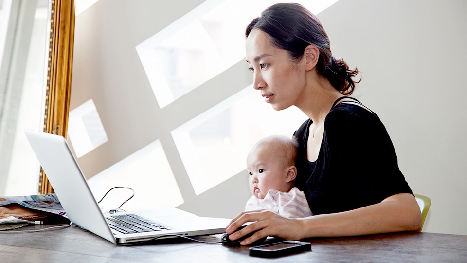 Mother holding baby while browsing on a laptop