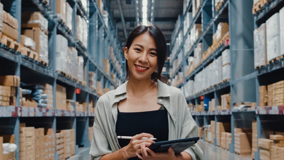 logisitcs manager smiling holding a tablet and pen standing in a distribution warehouse