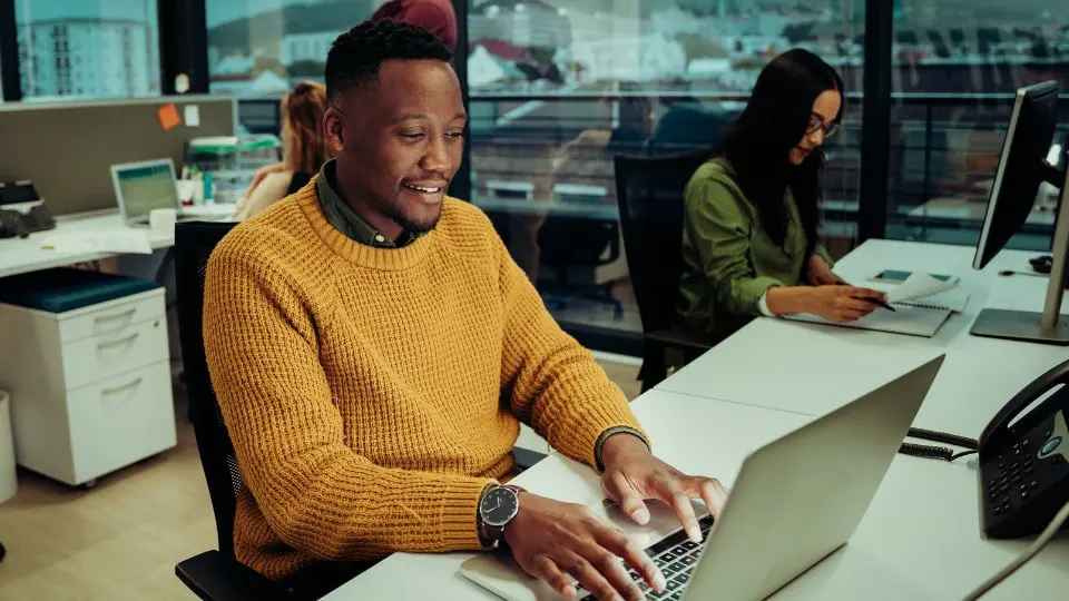 Profesional de negocios escribiendo en una computadora portátil sentado junto a un compañero de trabajo