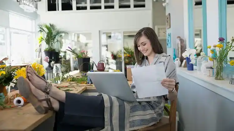 Vrouw zit glimlachend in een stoel terwijl ze naar de computer en een papieren factuur kijkt.