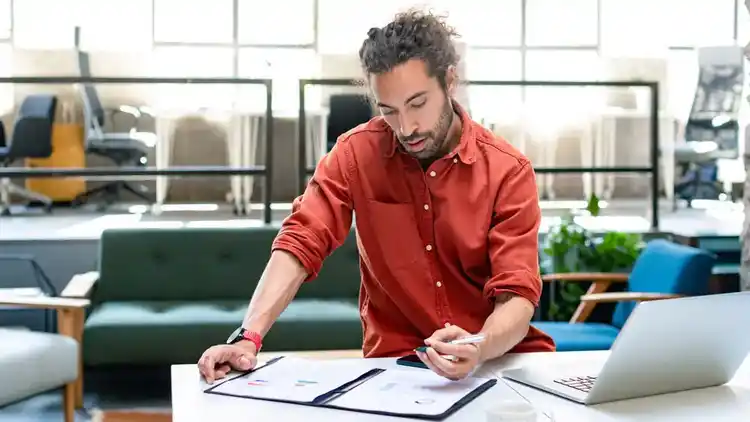 Zakenman staand aan bureau, betaalt rekeningen, heeft laptop open.