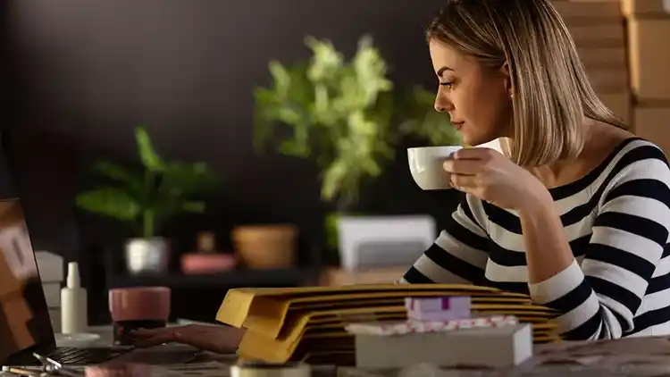 Woman drinking coffee and using her laptop.