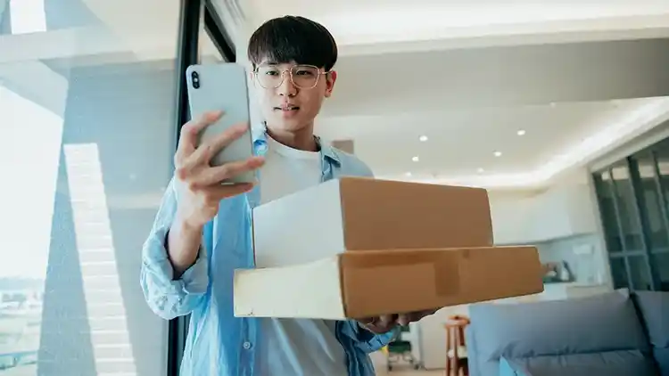 a person checking their phone while holding two boxes