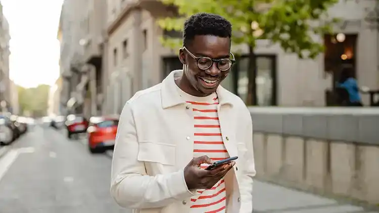 Osoba se venku přihlašuje pomocí mobilního telefonu na web U-P-S.com, aby nastavila uložení zásilky.