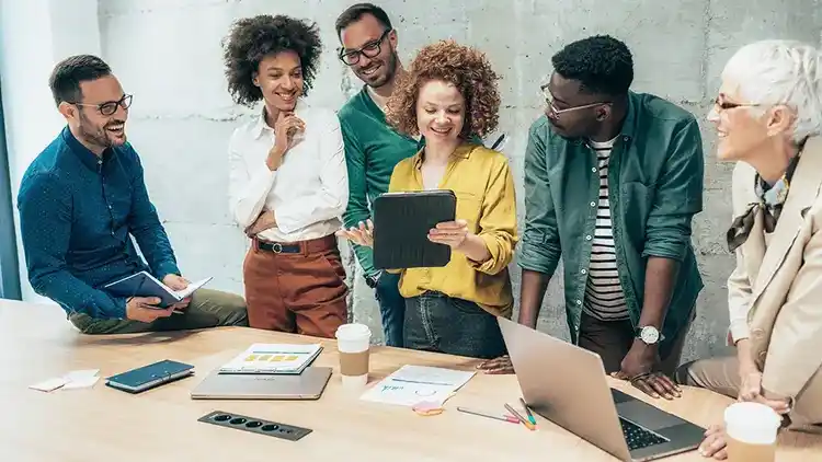 Group of 6 coworkers standing around a conference table working together.