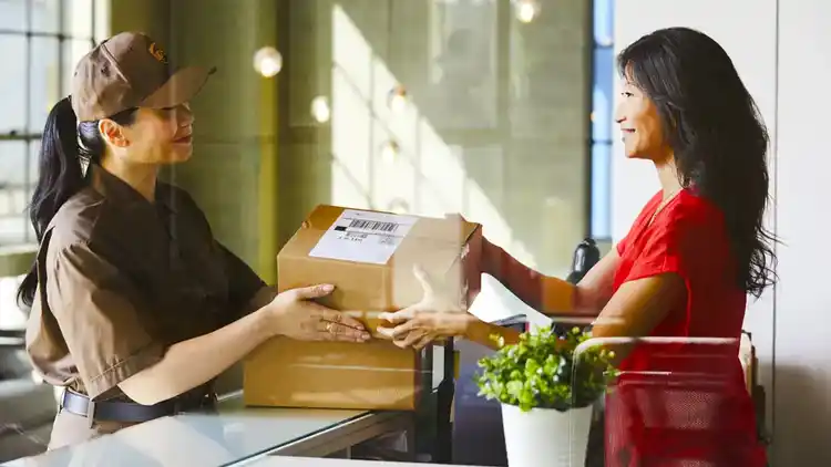 Close up of a desk with Christmas holiday lights and person’s hand on a laptop and holding a parcel.